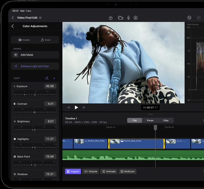 iPad Pro, face avant, bordure d’écran noire, écran affichant une app de montage vidéo avec l’image d’une personne portant une veste bleue et des pantalons à imprimé noir et blanc, panneau d’ajustement des couleurs ouvert sur la gauche avec plusieurs effets vidéo et curseurs, et une timeline dans la partie inférieure avec de multiples plans vidéo et pistes audio