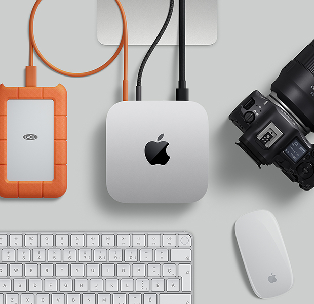 Vue en plongée d’un Mac mini argent sur un bureau, branché à un disque dur externe, à côté d’un Magic Keyboard blanc et argent, d’une Magic Mouse blanche et d’un appareil photo