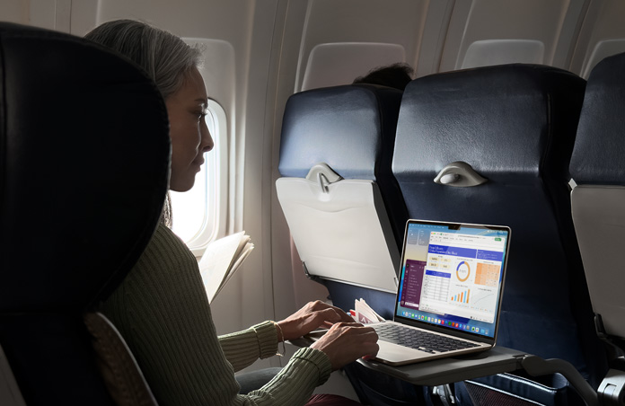 A person working on their MacBook Air while in an airplane seat