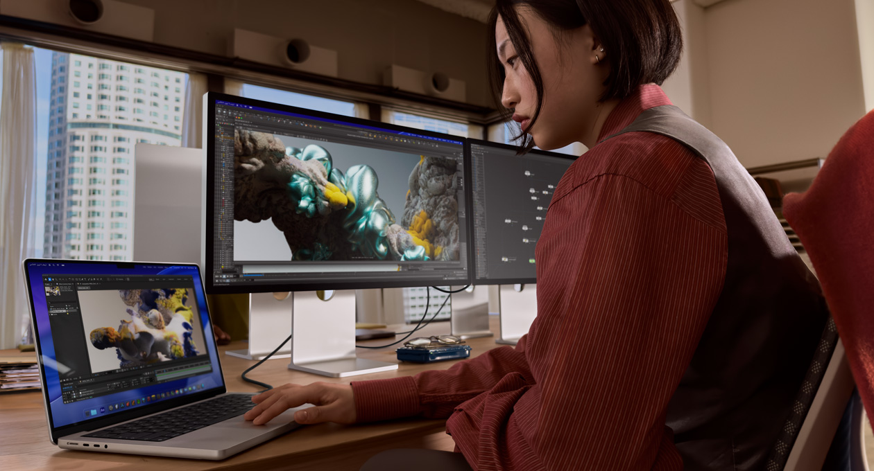 سيدة في مكتب تعمل على لابتوب MacBook متصل بشاشة Studio Display XDR عبر منفذ ثندربولت 5