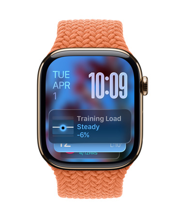 金色鈦金屬 Apple Watch 配上柑橘色編織錶帶，錶面的左上角顯示日期，右上角是以數字疊放方式顯示的時間，下方則是訓練負荷量小工具，全以半透明的 Liquid Glass 設計呈現