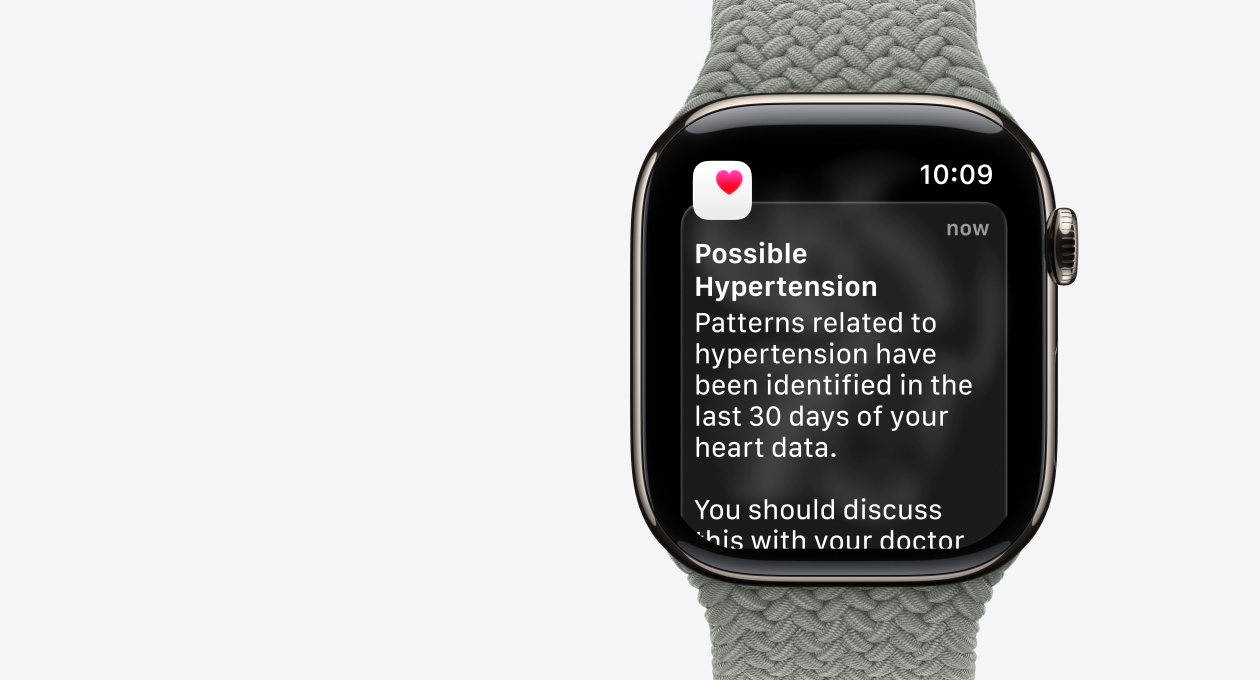 Apple Watch Series 11, natural colour, titanium case, possible hypertension notification, pink heart in white box, right side exterior, Digital Crown, band, green grey Braided Solo Loop