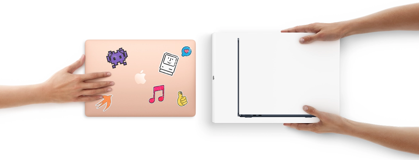 一隻手將一部外殼貼有貼紙的 MacBook 滑向前方，另一邊有兩隻手拿著全新盒裝的 MacBook