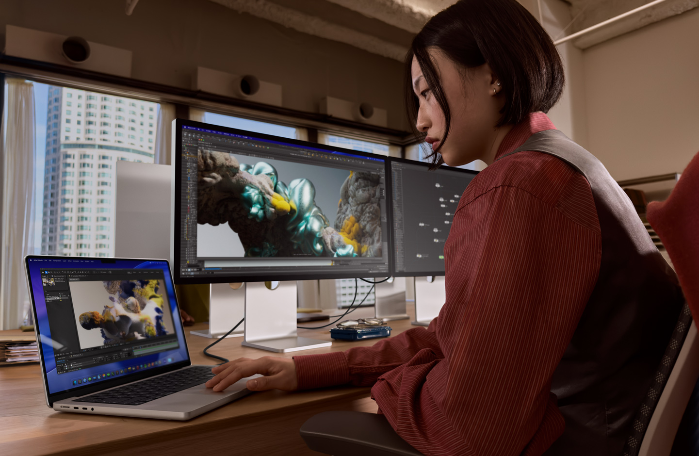 Людина в офісі працює на ноутбуку MacBook, підключеному до монітора Studio Display XDR через порт Thunderbolt 5