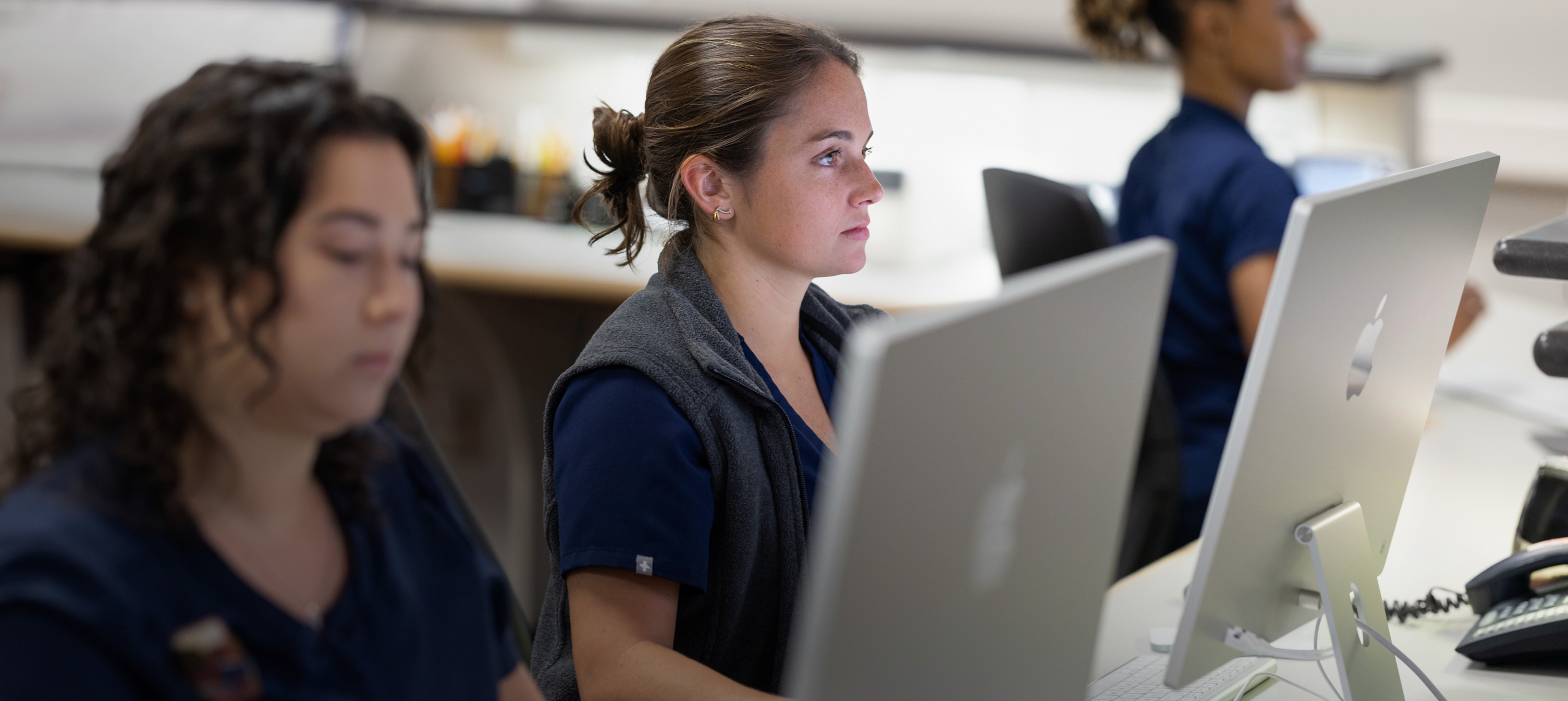 Trois infirmières travaillent derrière des écrans d’iMac.
