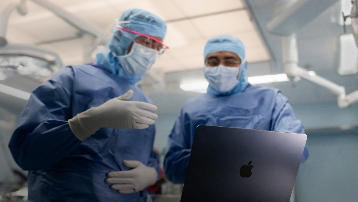 Deux chirurgiens échangent en regardant l’écran d’un MacBook Pro au bloc opératoire.