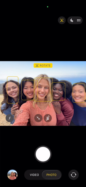 iPhone 17 Pro ekrāns, kurā redzama Center Stage funkcija bildēm un iespēja uzņemt cilvēku grupas selfiju, sejas ir izceltas